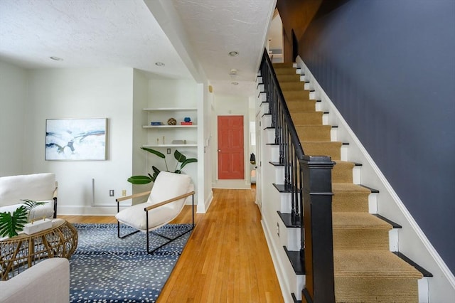 stairs with hardwood / wood-style floors, built in shelves, and a textured ceiling