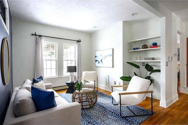 living area with wood-type flooring, a baseboard heating unit, a textured ceiling, and built in shelves