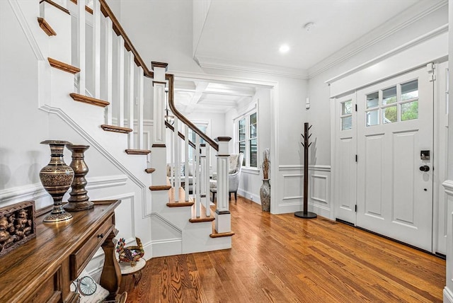 foyer featuring wood finished floors, coffered ceiling, stairway, a decorative wall, and ornamental molding