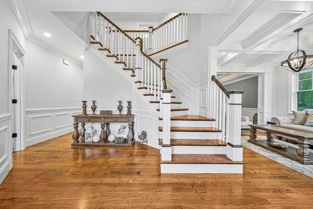 stairway with a decorative wall, wood finished floors, recessed lighting, crown molding, and an inviting chandelier