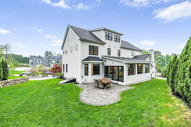 rear view of house featuring a patio, roof with shingles, a chimney, and a lawn
