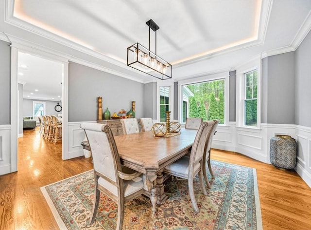 dining area featuring crown molding, light wood-type flooring, a decorative wall, and wainscoting