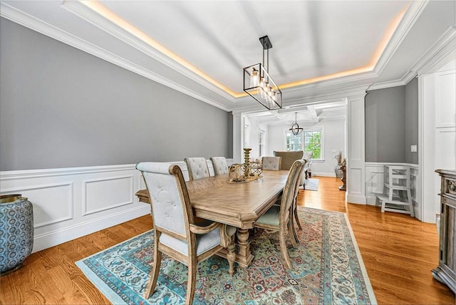 dining space featuring ornamental molding, an inviting chandelier, a tray ceiling, and a wainscoted wall