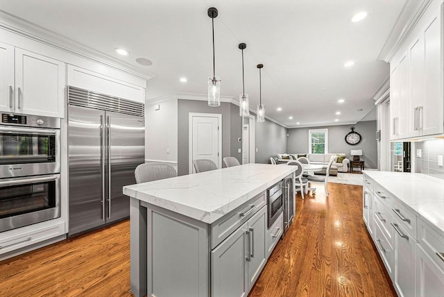 kitchen featuring built in appliances, gray cabinets, wood finished floors, ornamental molding, and open floor plan