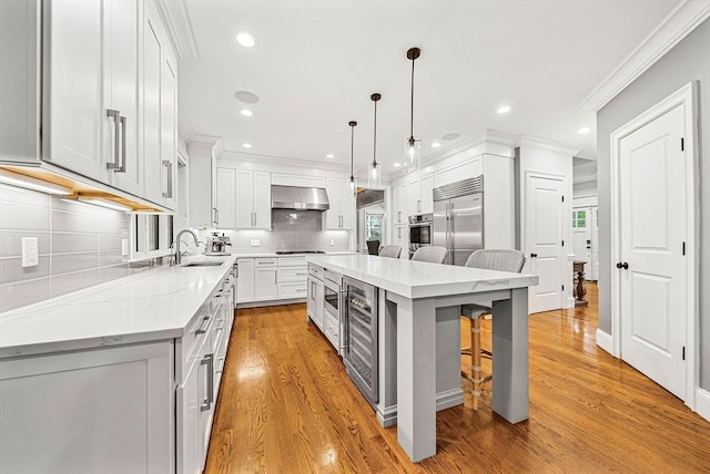 kitchen featuring wine cooler, a breakfast bar, a sink, wall chimney range hood, and stainless steel appliances