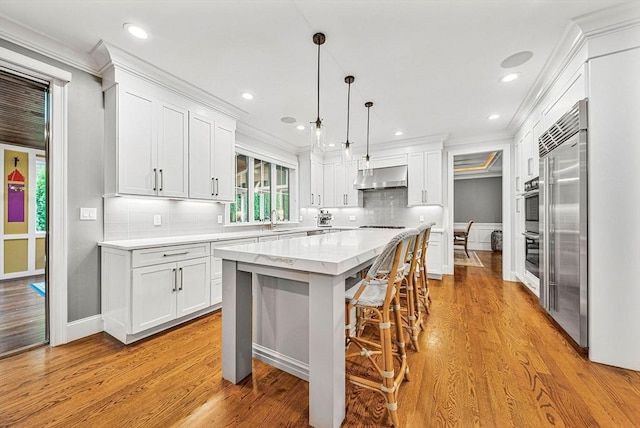 kitchen featuring ornamental molding, stainless steel appliances, white cabinets, and wall chimney exhaust hood