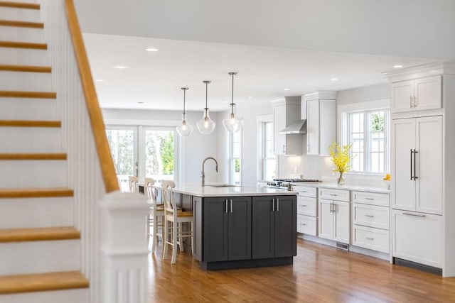 kitchen with a center island with sink, wood finished floors, light countertops, a sink, and white cabinets