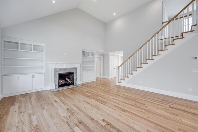 unfurnished living room featuring high vaulted ceiling, baseboards, wood finished floors, a high end fireplace, and stairway