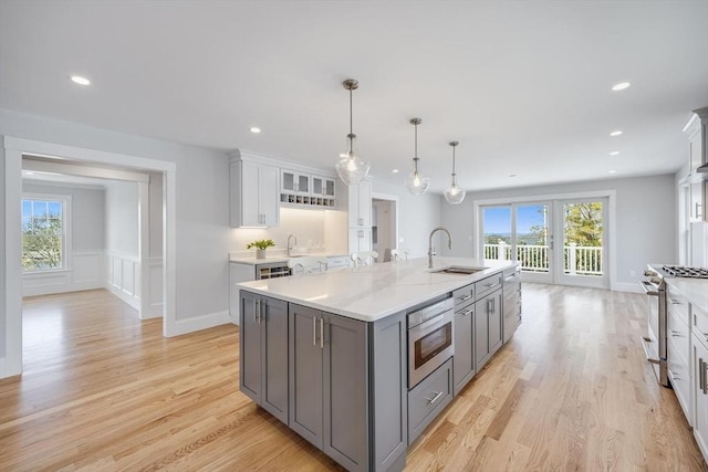kitchen featuring a sink, an island with sink, stainless steel appliances, white cabinetry, and gray cabinetry