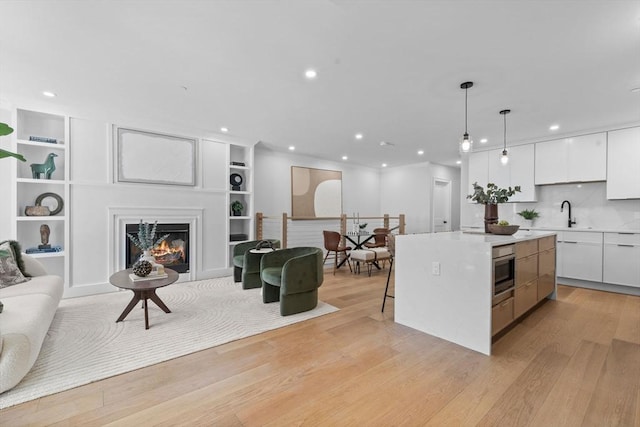 kitchen featuring a center island, light wood-style flooring, a warm lit fireplace, white cabinetry, and modern cabinets