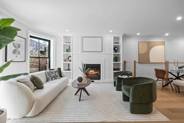 living area featuring built in shelves, wood finished floors, recessed lighting, a warm lit fireplace, and ornamental molding