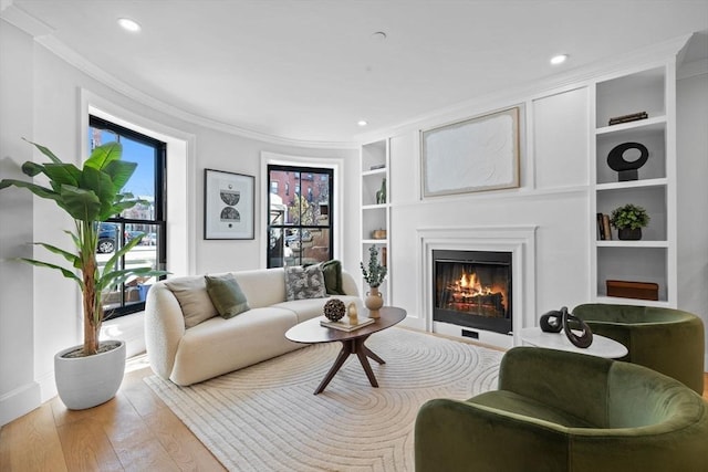 living room with built in features, a glass covered fireplace, wood finished floors, recessed lighting, and crown molding