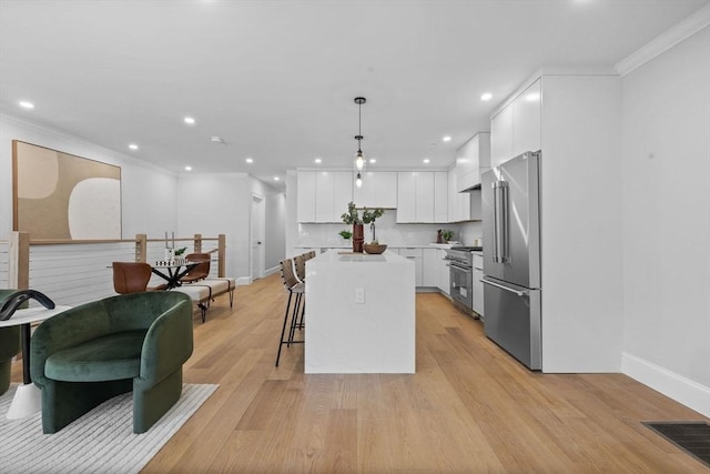 kitchen with light wood finished floors, a kitchen island, ornamental molding, white cabinets, and high end appliances