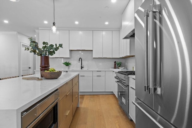 kitchen with tasteful backsplash, decorative light fixtures, premium appliances, light wood-style flooring, and a sink