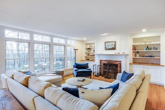 living area with light wood finished floors, a brick fireplace, built in features, and recessed lighting