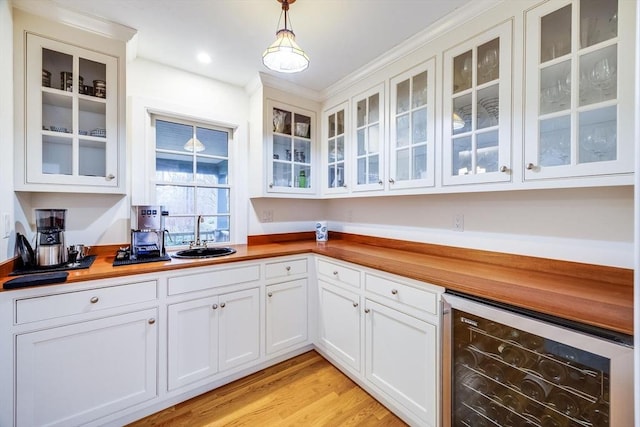 kitchen with white cabinets, wine cooler, hanging light fixtures, light wood-type flooring, and a sink