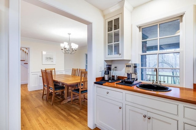 kitchen with crown molding, light wood-style floors, glass insert cabinets, white cabinets, and a sink