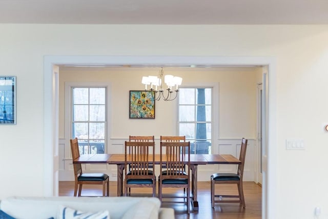 dining area with a wainscoted wall, a notable chandelier, a decorative wall, and wood finished floors