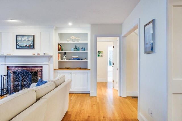 living room with built in shelves, a fireplace, light wood-style flooring, and baseboards