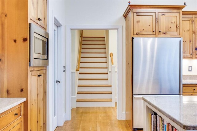 kitchen with appliances with stainless steel finishes, light wood-style flooring, and light stone counters