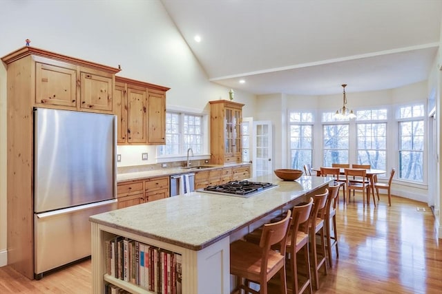 kitchen with light wood finished floors, appliances with stainless steel finishes, a kitchen island, a sink, and light stone countertops