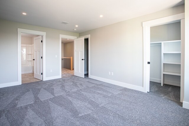 unfurnished bedroom featuring ensuite bath, a closet, a walk in closet, and carpet floors