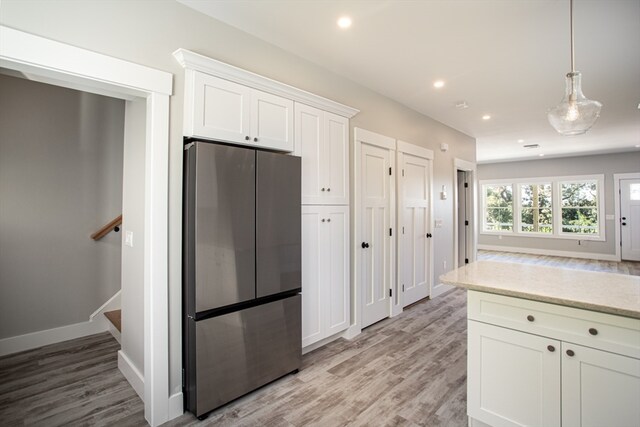 kitchen with hanging light fixtures, light stone countertops, light hardwood / wood-style floors, white cabinetry, and stainless steel fridge