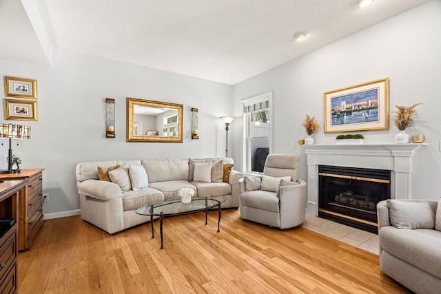 living room featuring baseboards, a fireplace with flush hearth, and light wood-style flooring