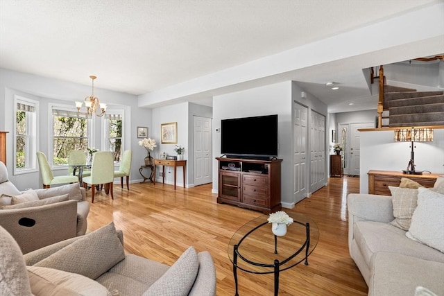 living room featuring an inviting chandelier, baseboards, stairway, and light wood finished floors