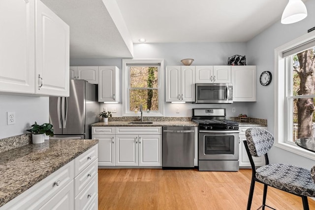 kitchen with appliances with stainless steel finishes, a sink, white cabinets, light wood finished floors, and stone counters