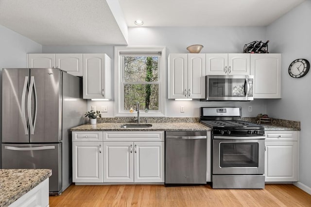 kitchen featuring a sink, light stone counters, stainless steel appliances, and white cabinetry