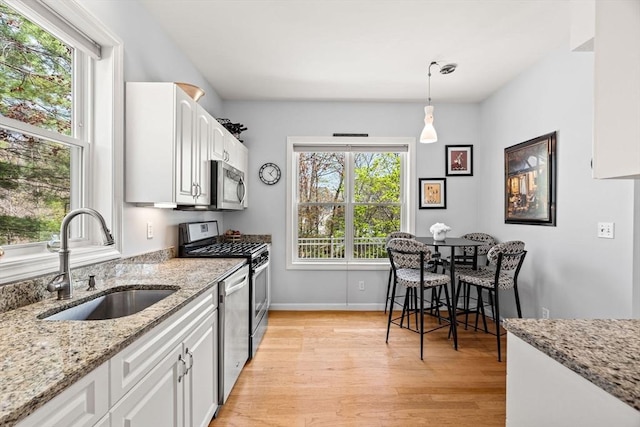 kitchen featuring pendant lighting, a sink, light wood finished floors, stainless steel appliances, and white cabinetry