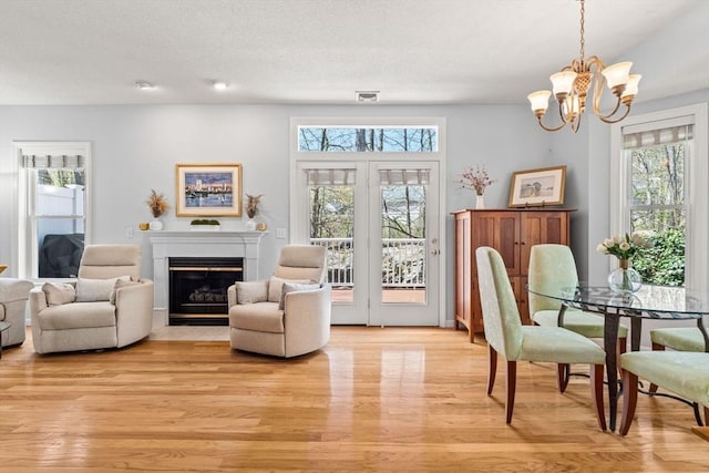 sitting room featuring a notable chandelier, a fireplace with flush hearth, light wood finished floors, and visible vents