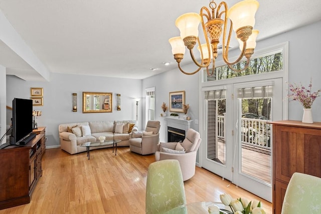 living room featuring an inviting chandelier, a glass covered fireplace, and light wood-style flooring