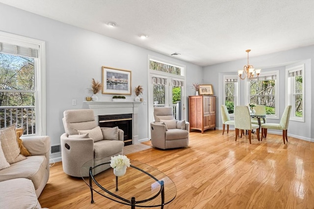 living area featuring light wood finished floors, a chandelier, baseboards, a fireplace with flush hearth, and visible vents