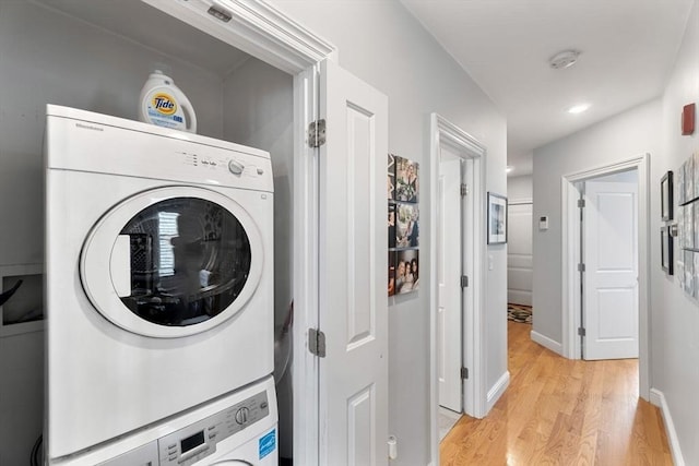 washroom featuring stacked washer / dryer, laundry area, baseboards, and light wood-style floors