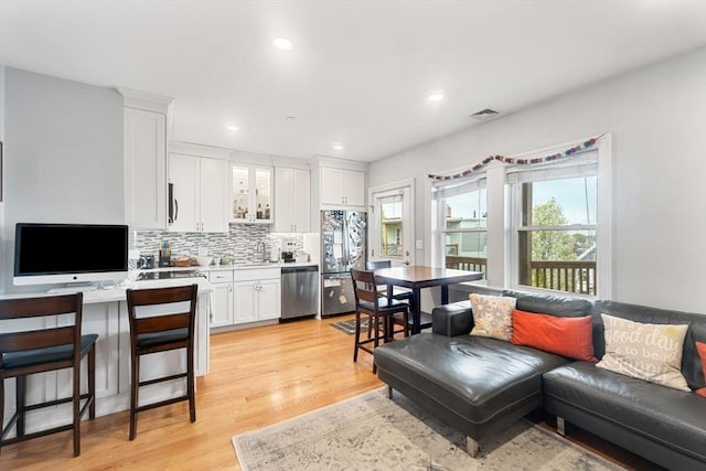 interior space with appliances with stainless steel finishes, white cabinets, backsplash, light countertops, and light wood-style floors