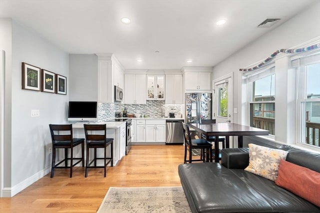 kitchen with light wood-style flooring, white cabinetry, decorative backsplash, light countertops, and appliances with stainless steel finishes