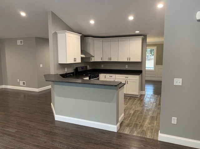 kitchen with wall chimney exhaust hood, white cabinetry, dark hardwood / wood-style floors, kitchen peninsula, and stove