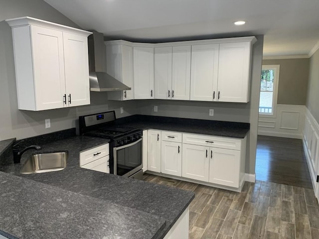 kitchen featuring stainless steel gas range oven, sink, white cabinets, and wall chimney exhaust hood