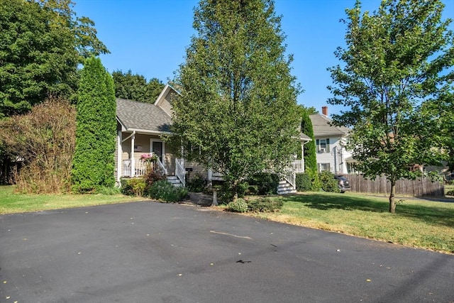 view of property hidden behind natural elements featuring a front lawn, fence, and covered porch