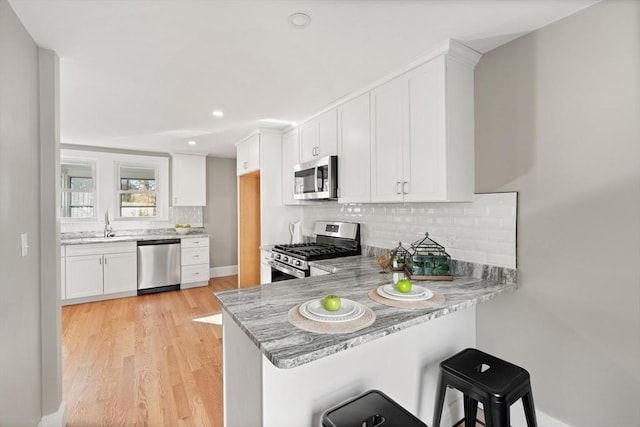 kitchen featuring white cabinetry, kitchen peninsula, stainless steel appliances, light stone countertops, and a breakfast bar