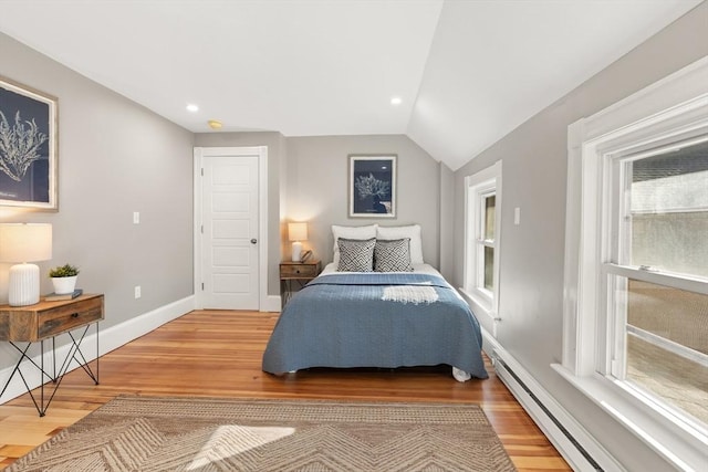 bedroom with a baseboard heating unit, vaulted ceiling, multiple windows, and hardwood / wood-style floors