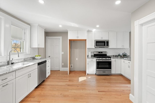 kitchen with white cabinetry, stainless steel appliances, decorative backsplash, sink, and light stone counters