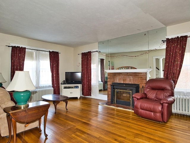 living room with wood-type flooring, radiator heating unit, and a brick fireplace