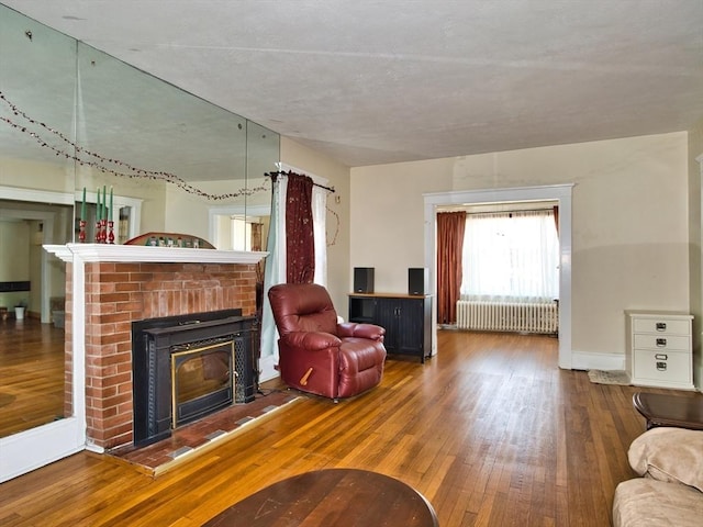 living room with hardwood / wood-style flooring, a brick fireplace, and radiator