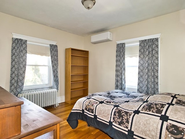 bedroom featuring hardwood / wood-style floors, radiator heating unit, and a wall unit AC