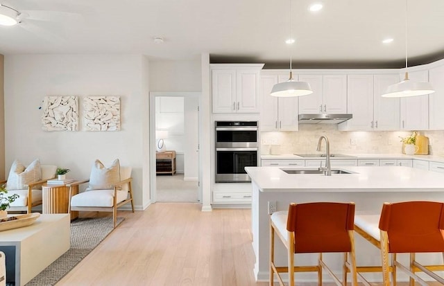 kitchen with white cabinetry, stainless steel double oven, decorative light fixtures, and light wood-type flooring