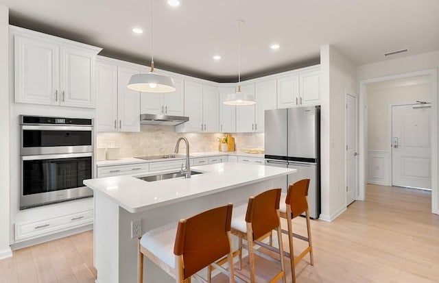 kitchen with backsplash, white cabinets, hanging light fixtures, light wood-type flooring, and appliances with stainless steel finishes