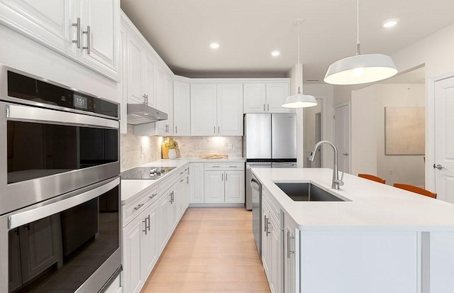 kitchen featuring white cabinets, a center island with sink, sink, hanging light fixtures, and stainless steel appliances